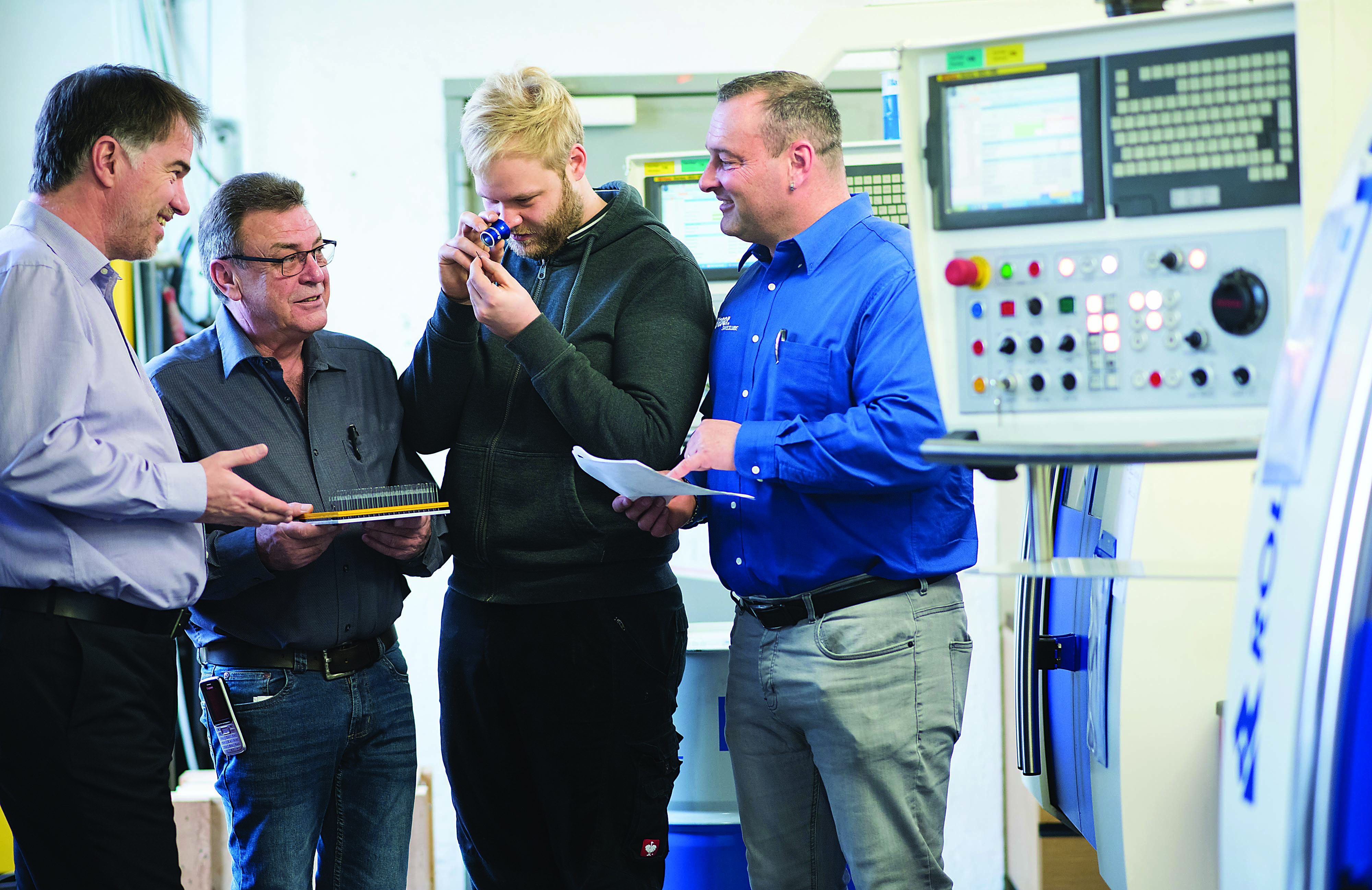 Werkzeugschleiferei Hugo Limmer Engineer Linus Erlacher (center right) examines a cutting tool with founder Hugo Limmer (center left) and Martin Reichhart, application engineer for Blaser Swisslube (far right), in front of a Rollomatic six-axis tool and cutter grinder. 